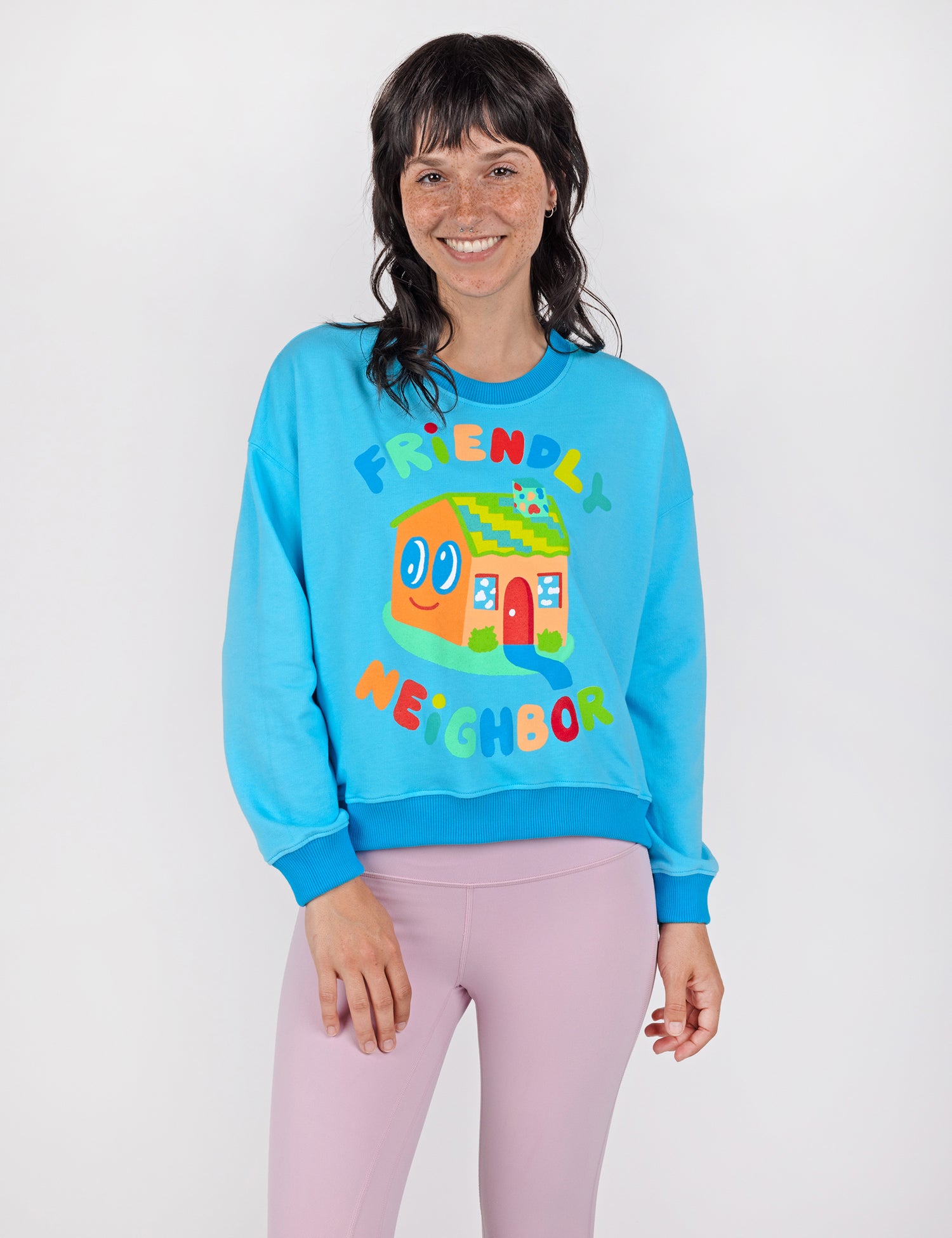 Woman wearing a blue crop crew sweatshirt with colorful letters and house design