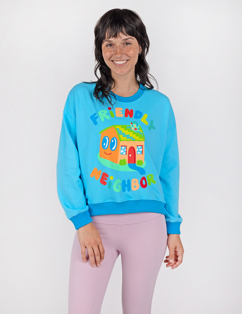 Woman wearing a blue crop crew sweatshirt with colorful letters and house design