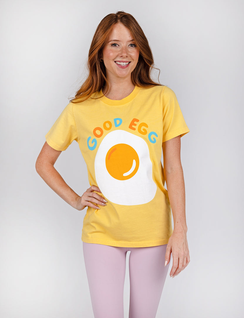 woman wearing yellow shirt with an egg design in the middle and colorful letters.