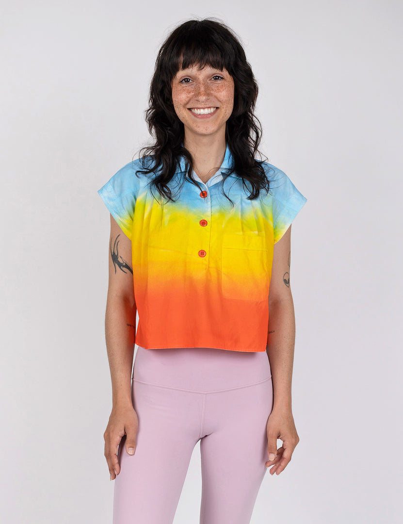 woman wearing a cropped half button down shirt in gradient designs of blue yellow and red orange.