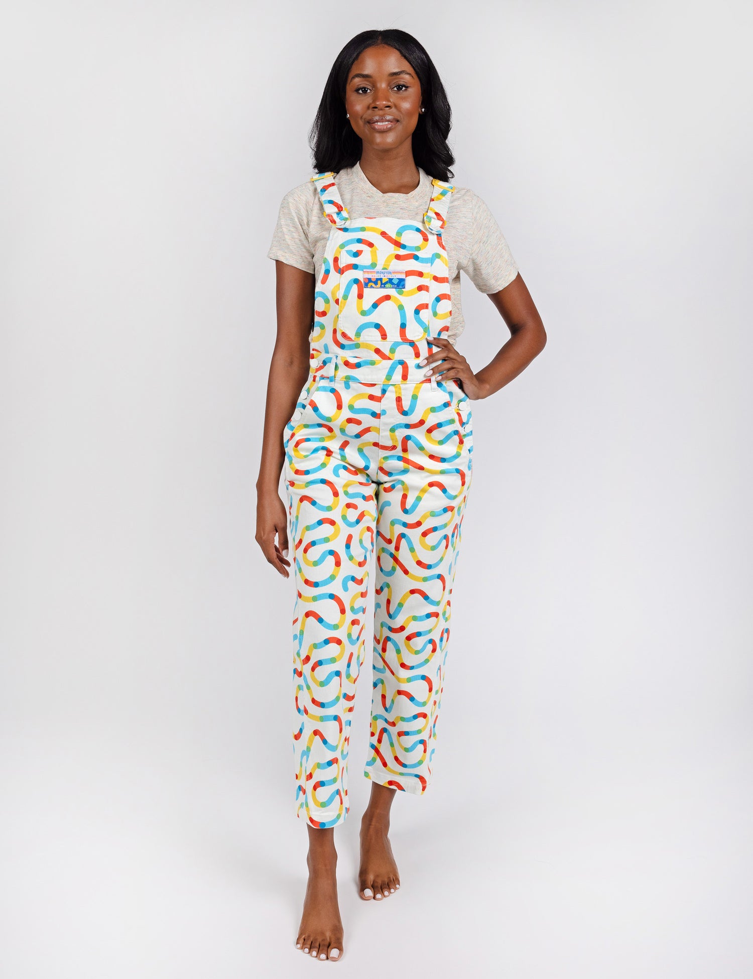 woman wearing white pants overalls with colorful squiggle designs.