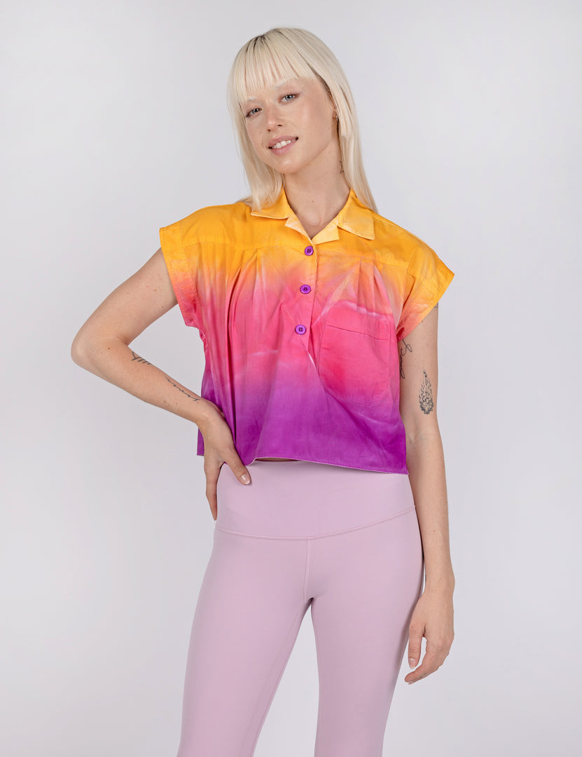 woman wearing a cropped half button down shirt in gradient designs of yellow pink and purple